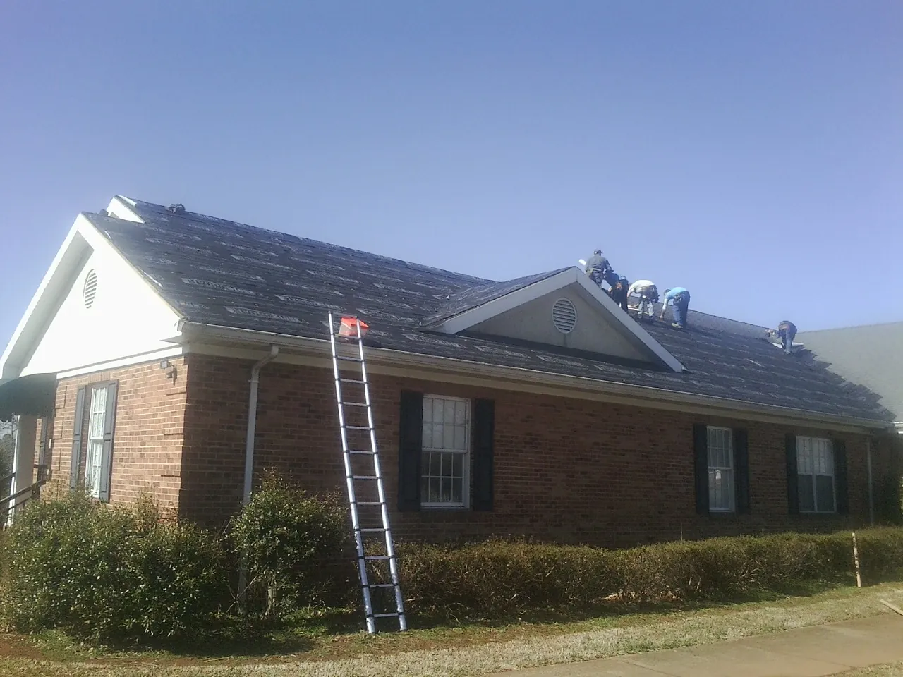 Crew tearing shingles off a brick ranch roof with a ladder set — Metal Roof Repair work by our crew in Swarthmore