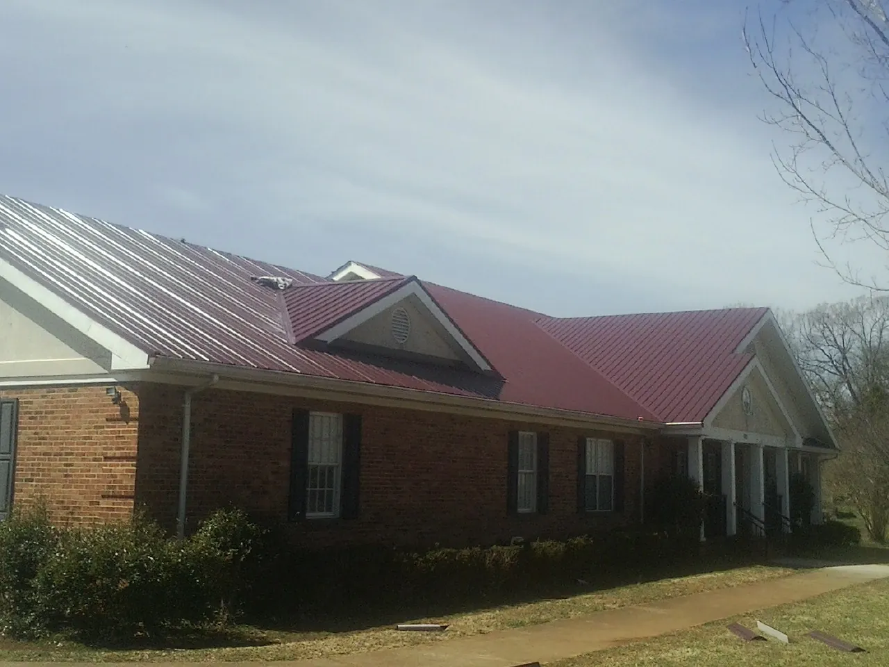 Red metal roof with gabled entries on a long brick building, from a Hail Damage Roof Repair job in Swarthmore