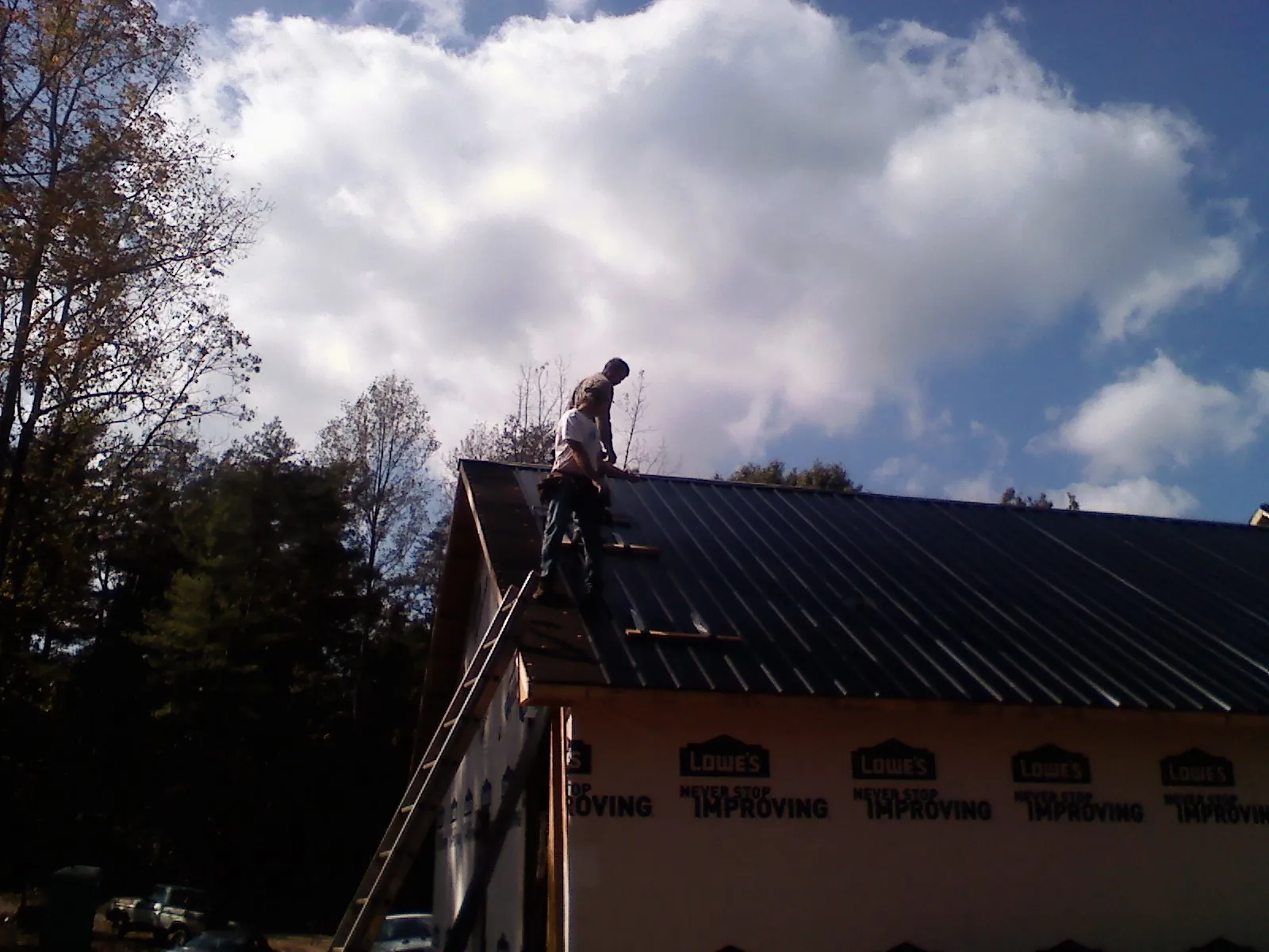 Roofer fastening dark metal panels high against a cloudy sky, from a Roof Inspection job in Swarthmore