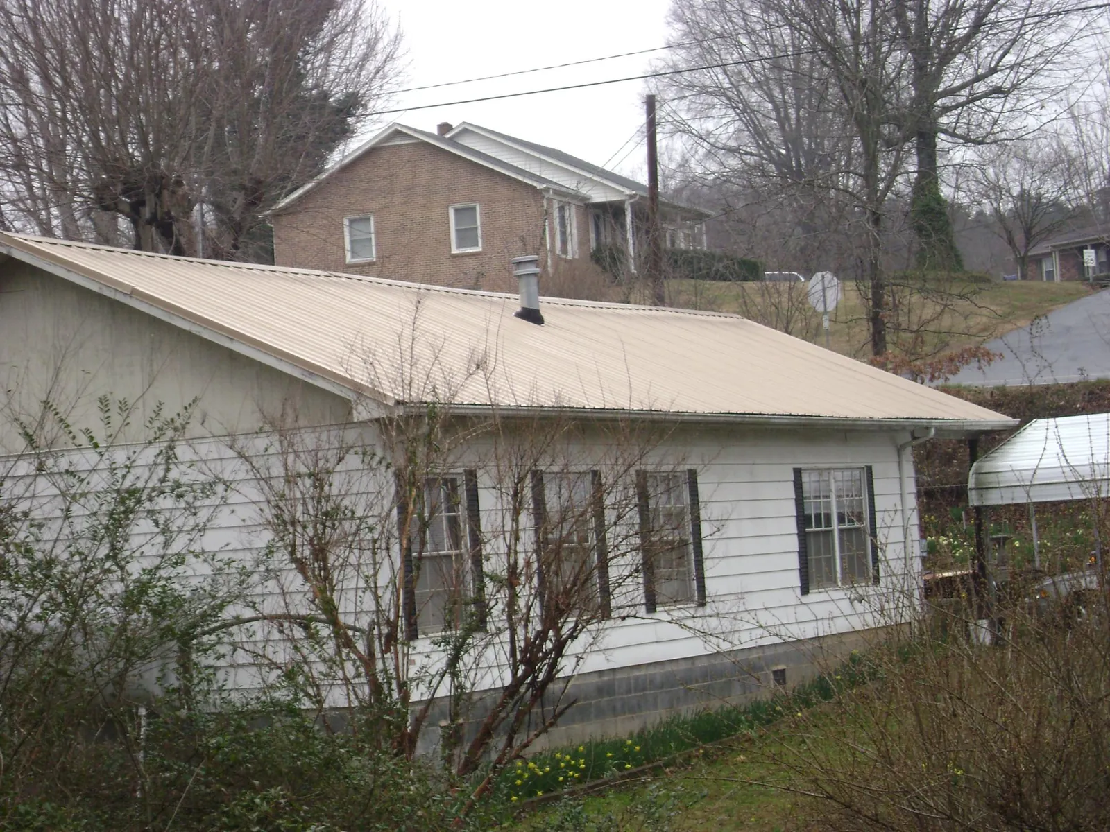 Tan metal roof on a white sided house set into a hillside — Commercial Roofing by Roofing Brothers in Swarthmore